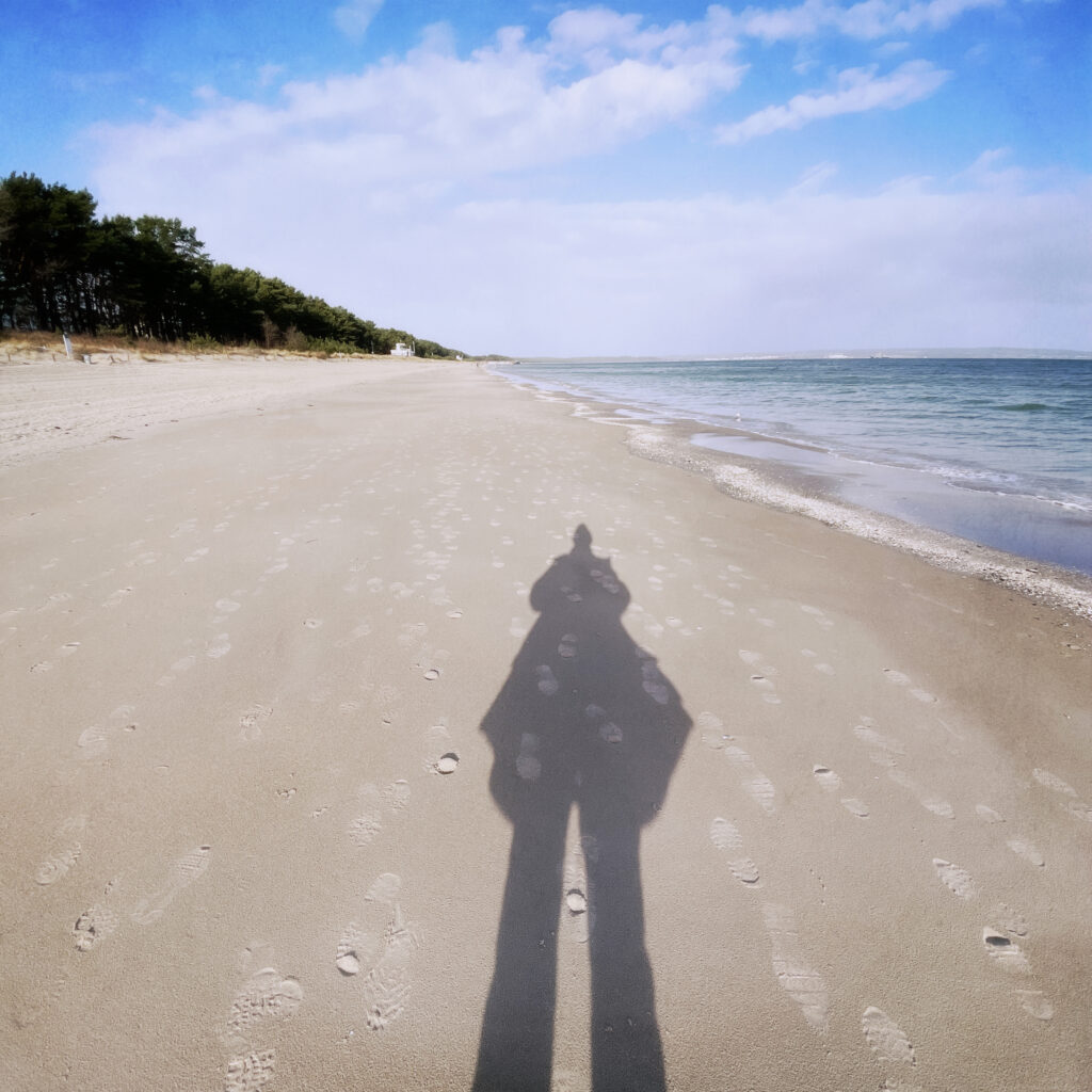A person casting a long shadow on the sandy beach of the baltic sea