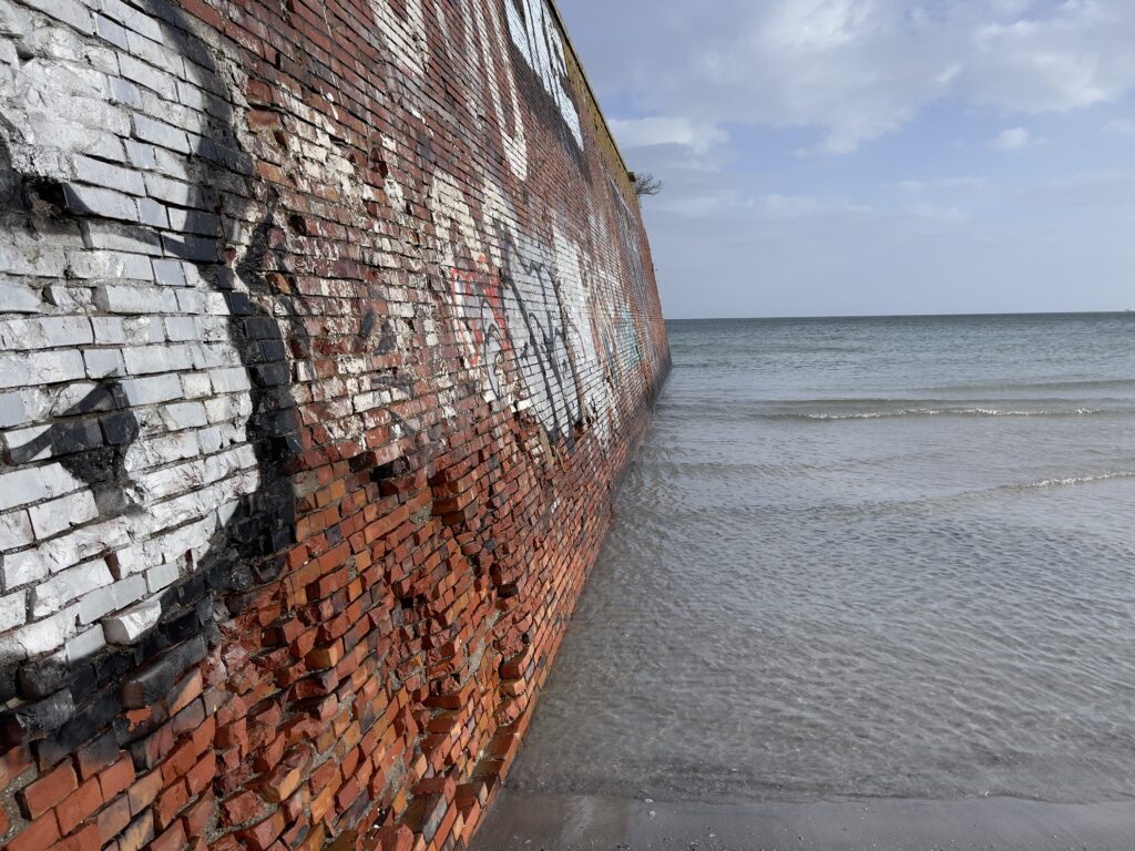 a red brick wall stretching into the baltic sea. The wall is partially covered with grafiti
