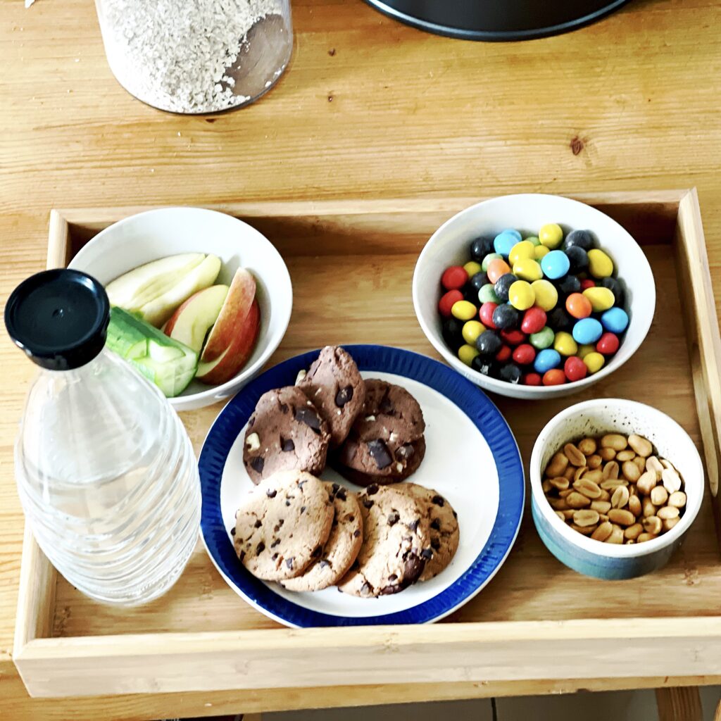 a tablet with a plate, 3 bowls and a water bottle. The plate contains cookies, the bowls M&Ms, apple slices, peanuts.