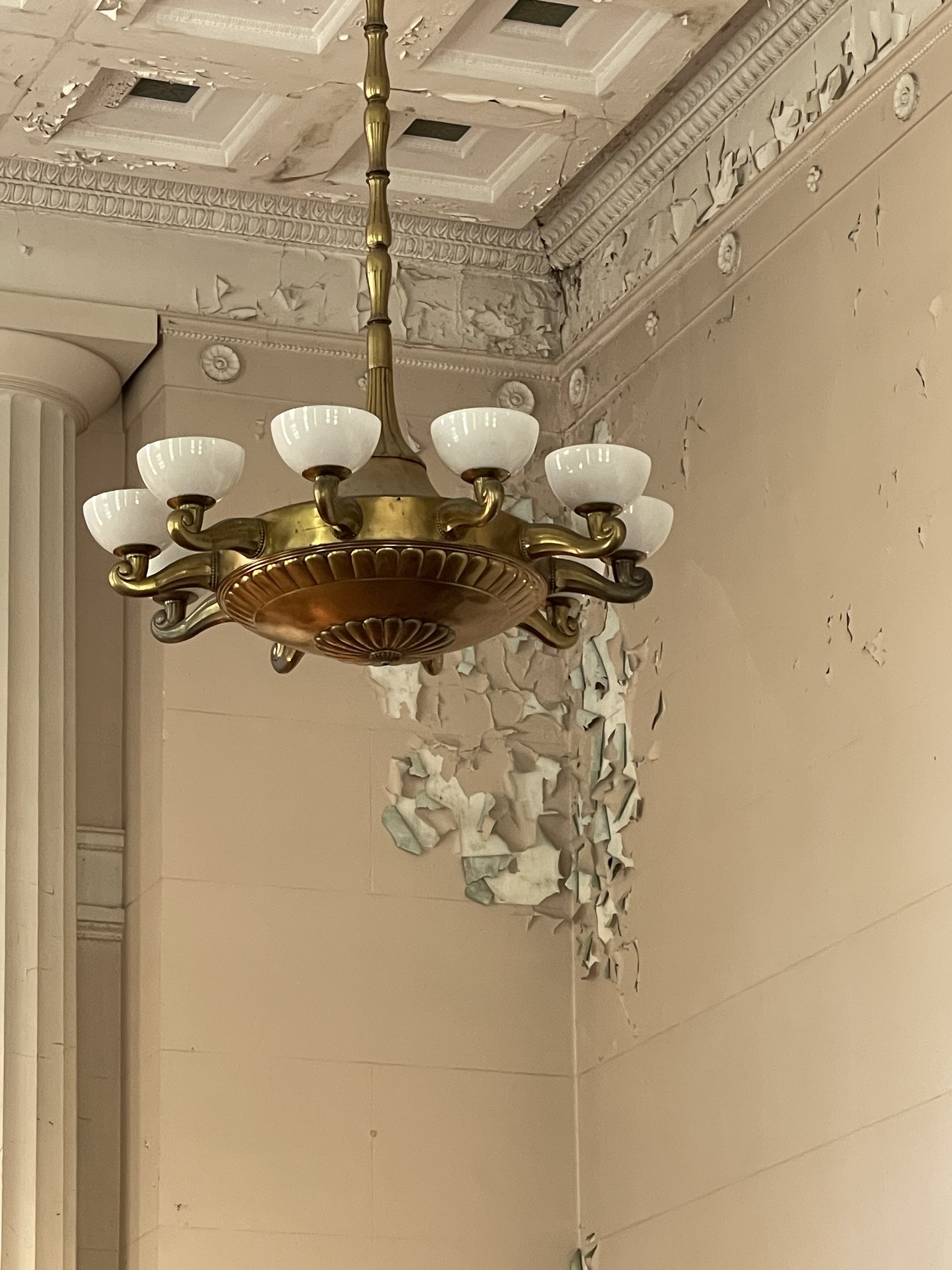Large, ornate chandelier hanging from a ceiling with peeling paint on the walls and ceiling.
