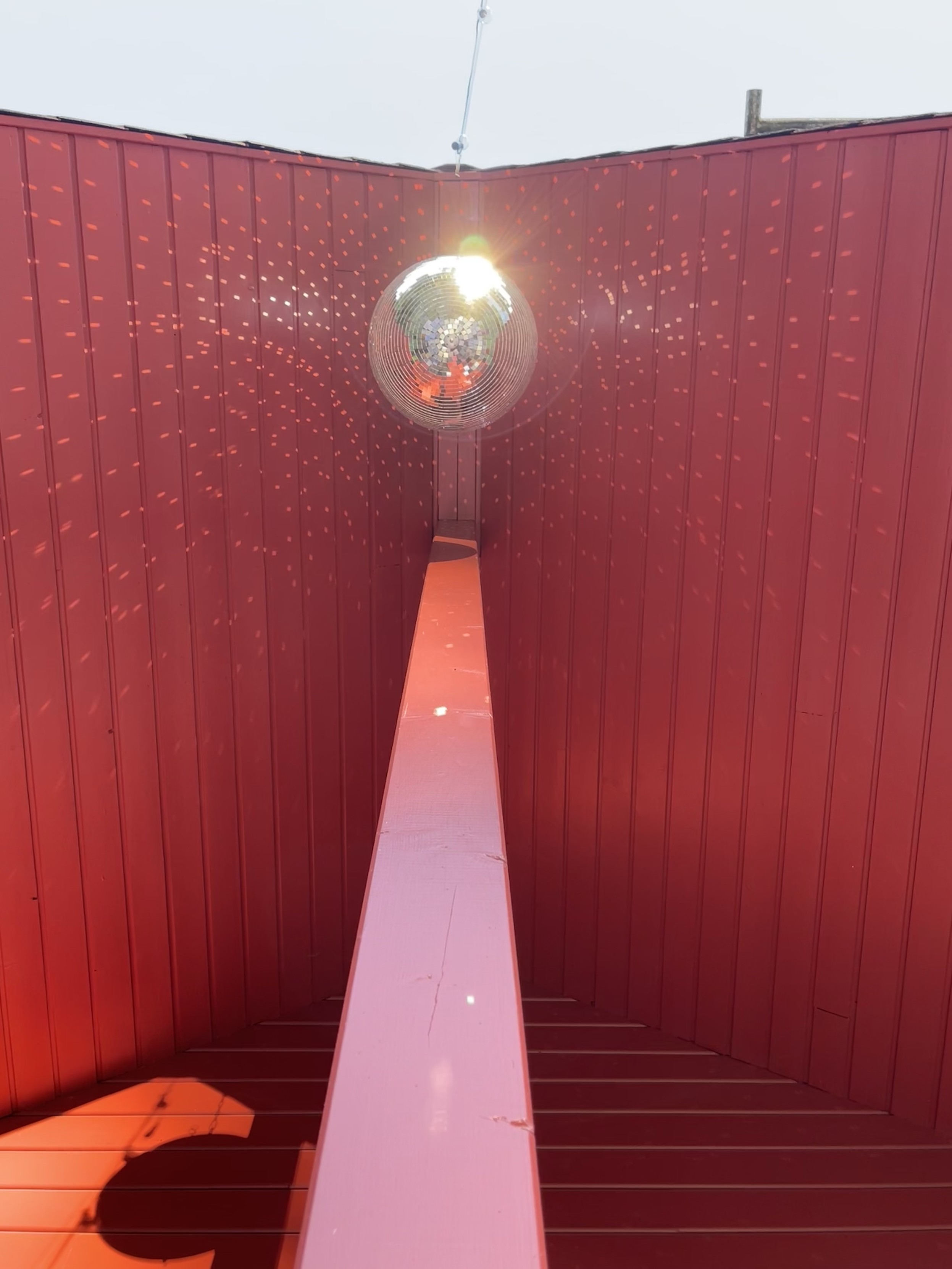 A disco ball hanging inside a red wooden ceiling structure, reflecting light and creating a pattern of small light dots on the walls.