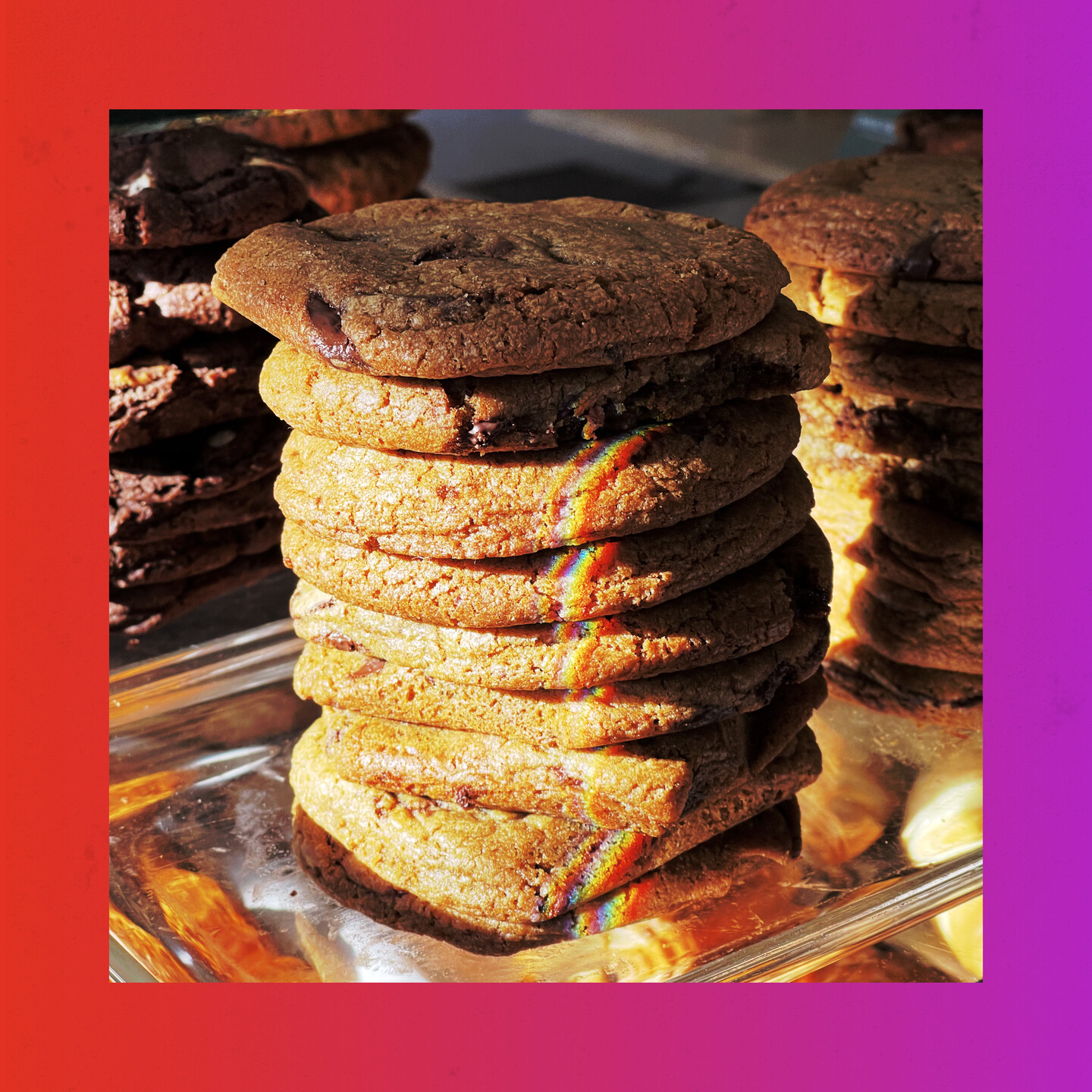 a Stack of chocolate chip cookies. there is refracted light shining on the cookies applying a small strip of rainbow colors on the side of the stack. 