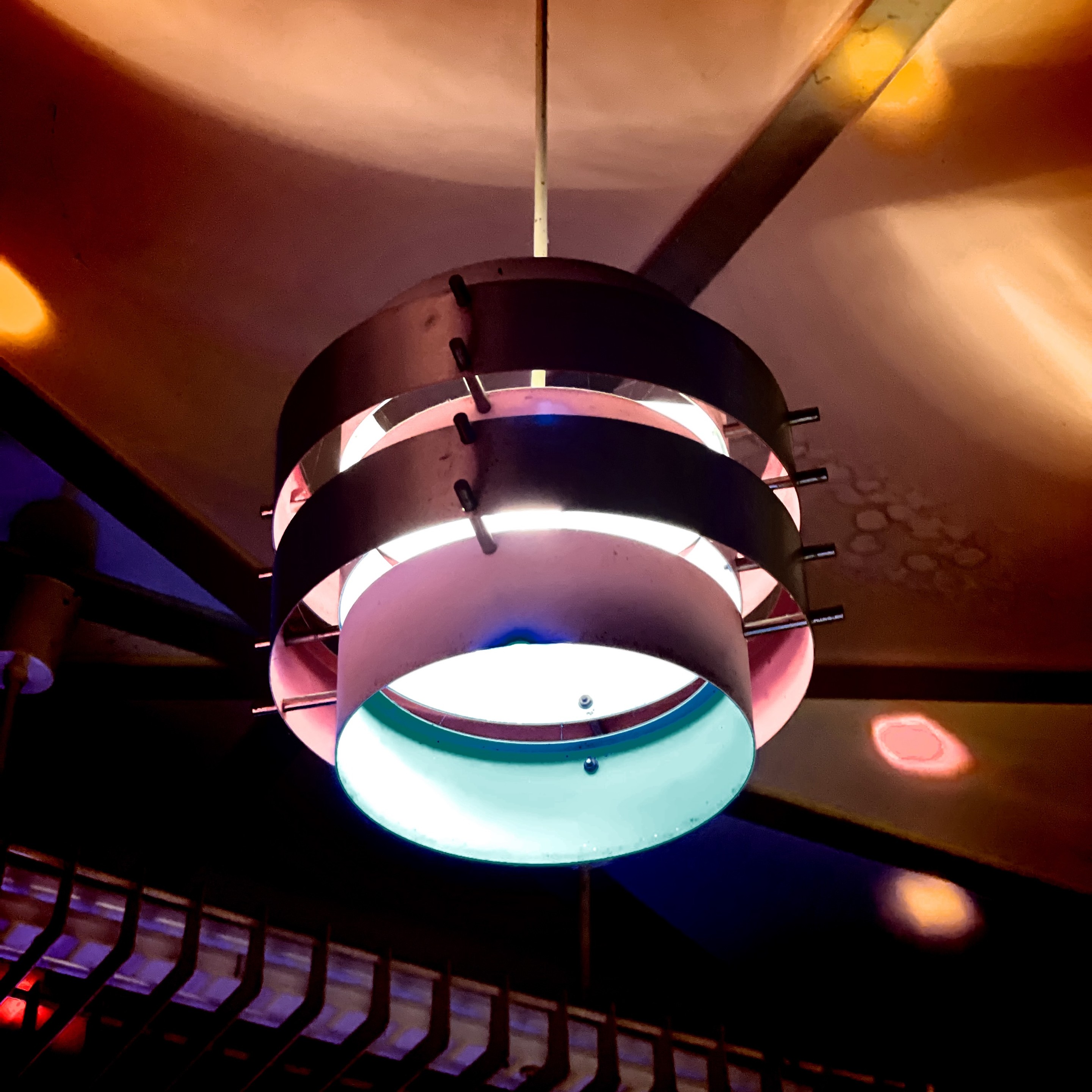Eine historische (DDR-) Hängelampe mit kreisförmigen Bändern und farbigem Licht, das an der Decke leuchtet.