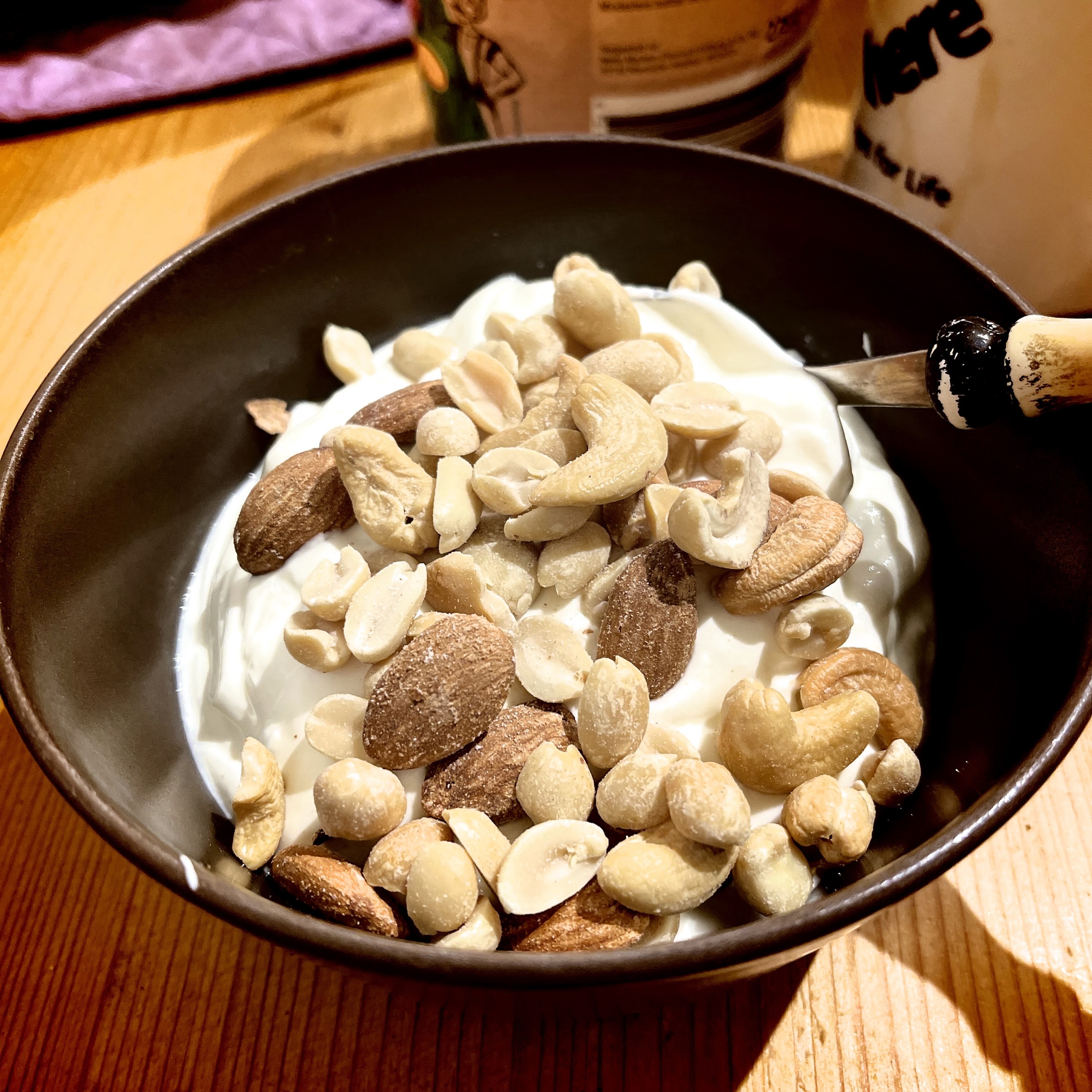 A bowl of yogurt with mixed nuts and a spoon on a wooden table.