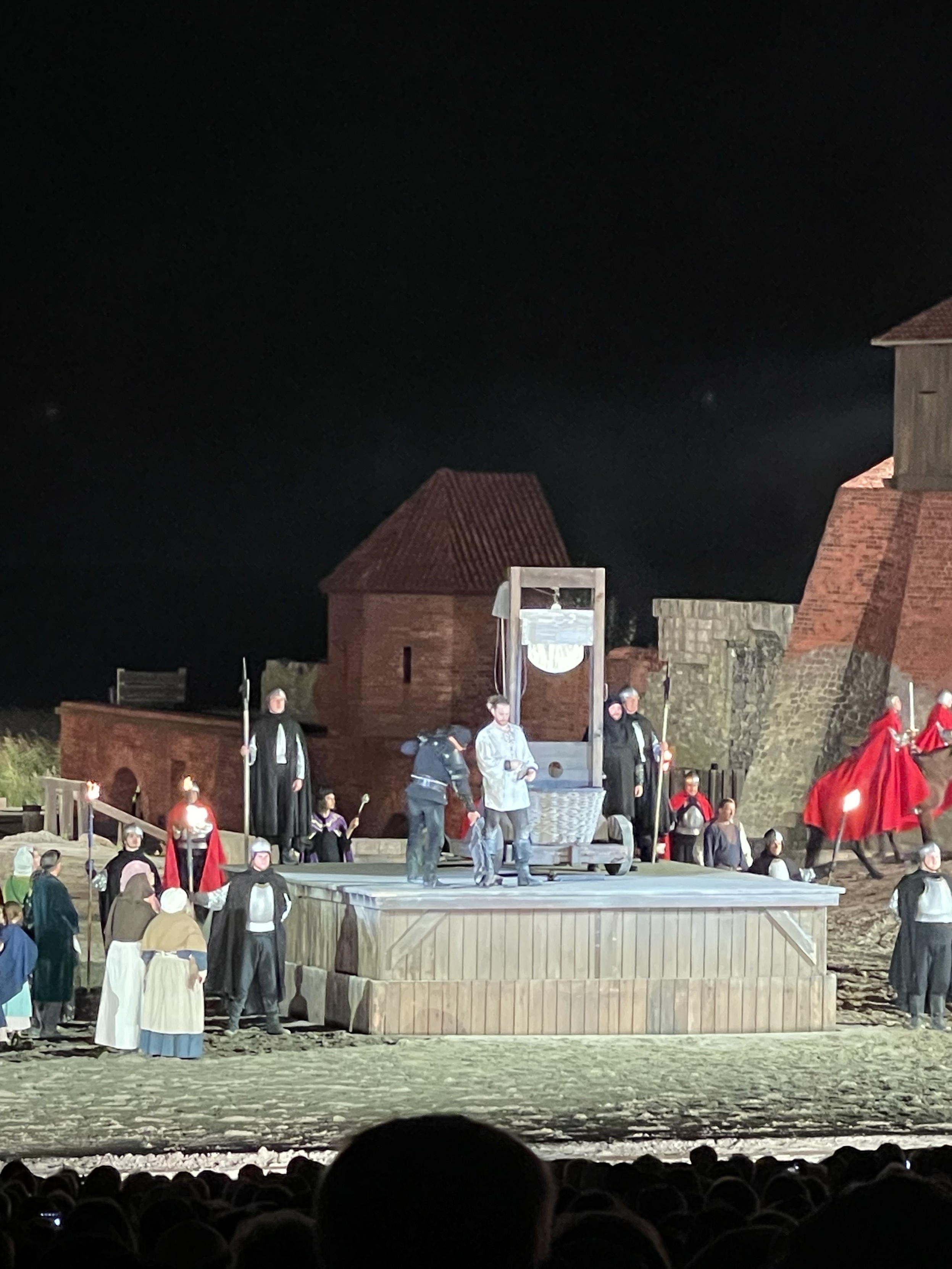 Theateraufführung im Freien mit Schauspielern in historischen Kostümen rund um eine Guillotine-Bühne.