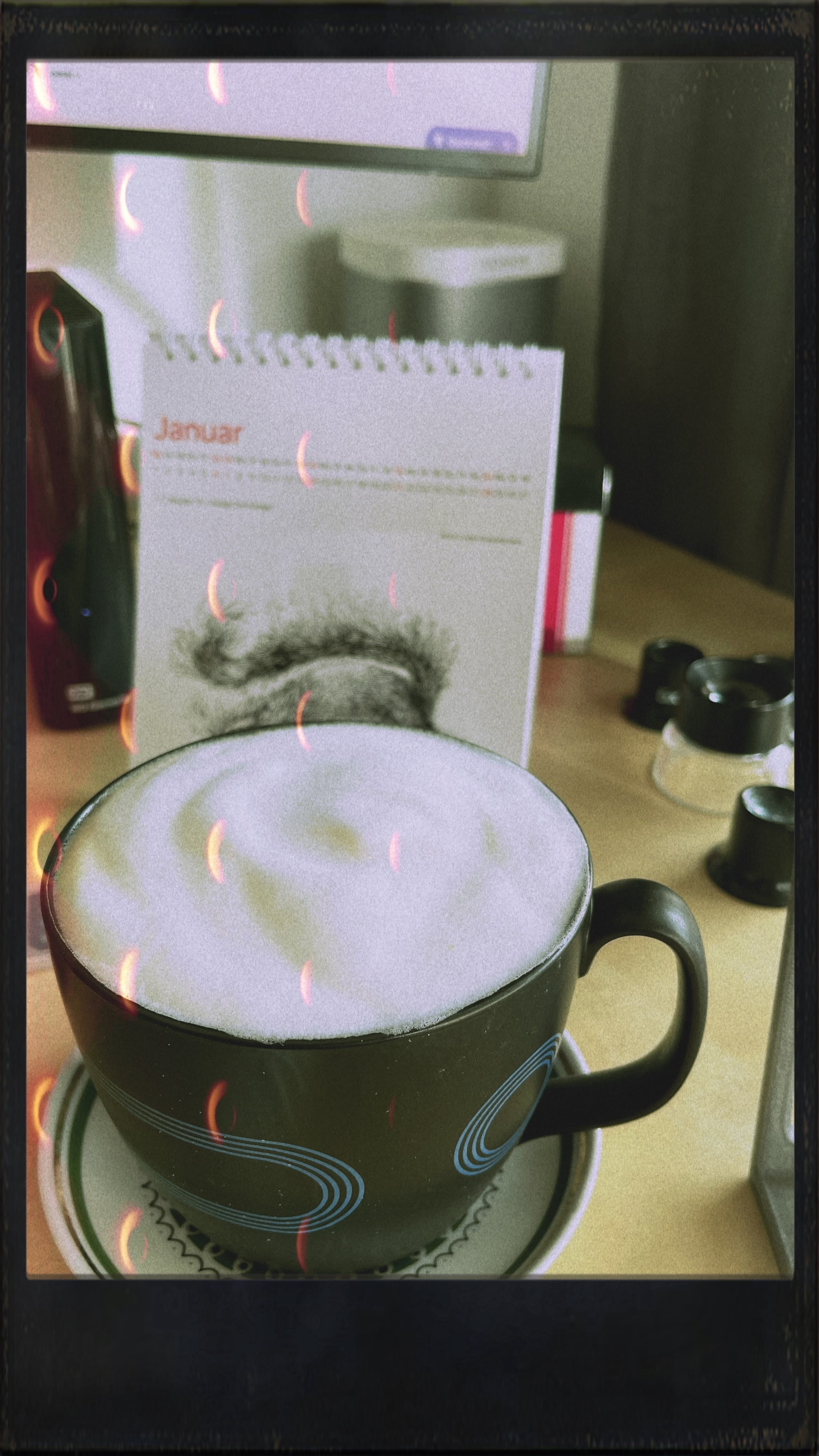 A cup of cappuccino on a saucer with a flip calendar showing January in the background. Vintage filter applied.