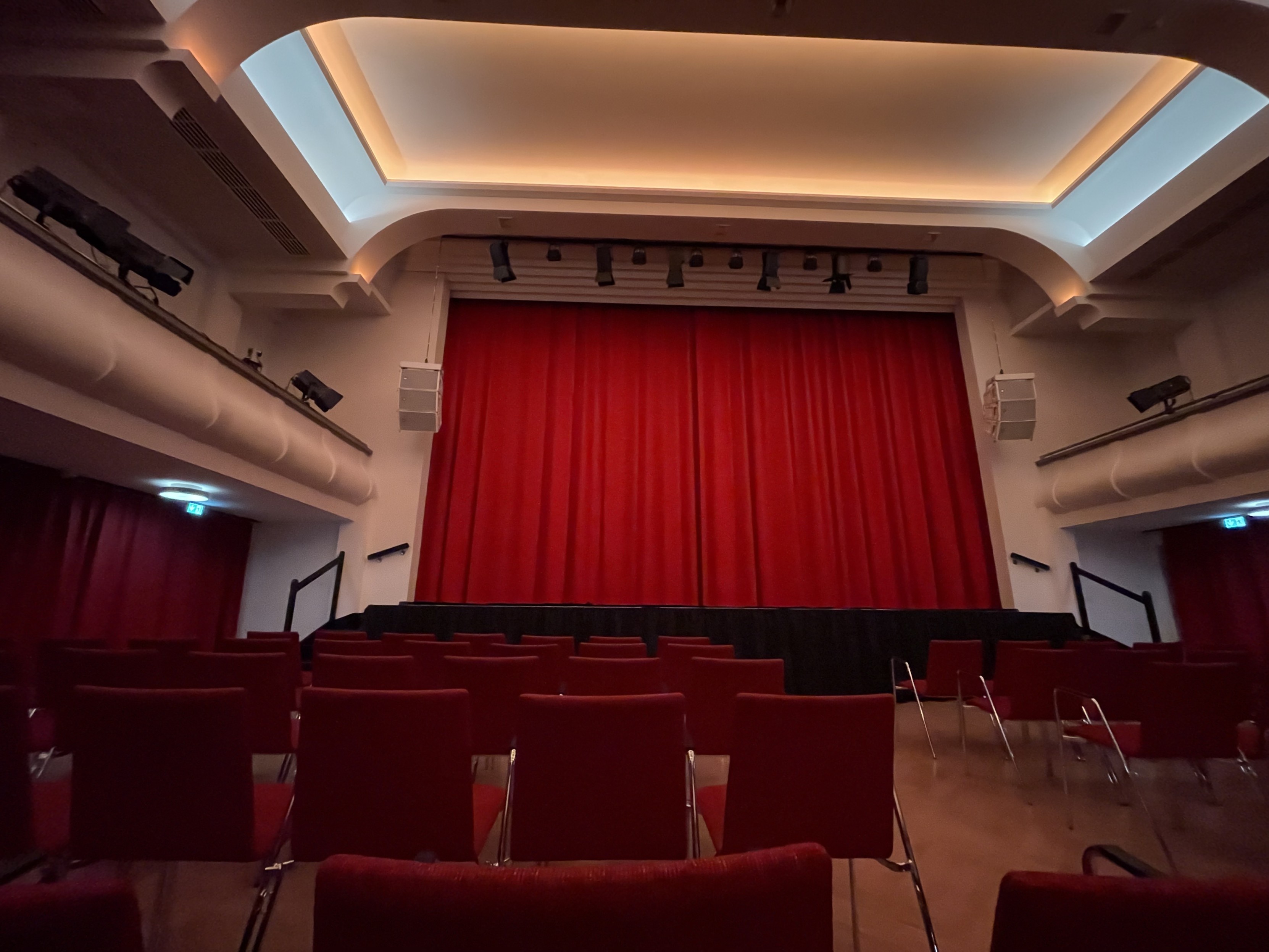 Leeres Theater mit roten Sitzen und einem geschlossenen roten Vorhang auf der Bühne.