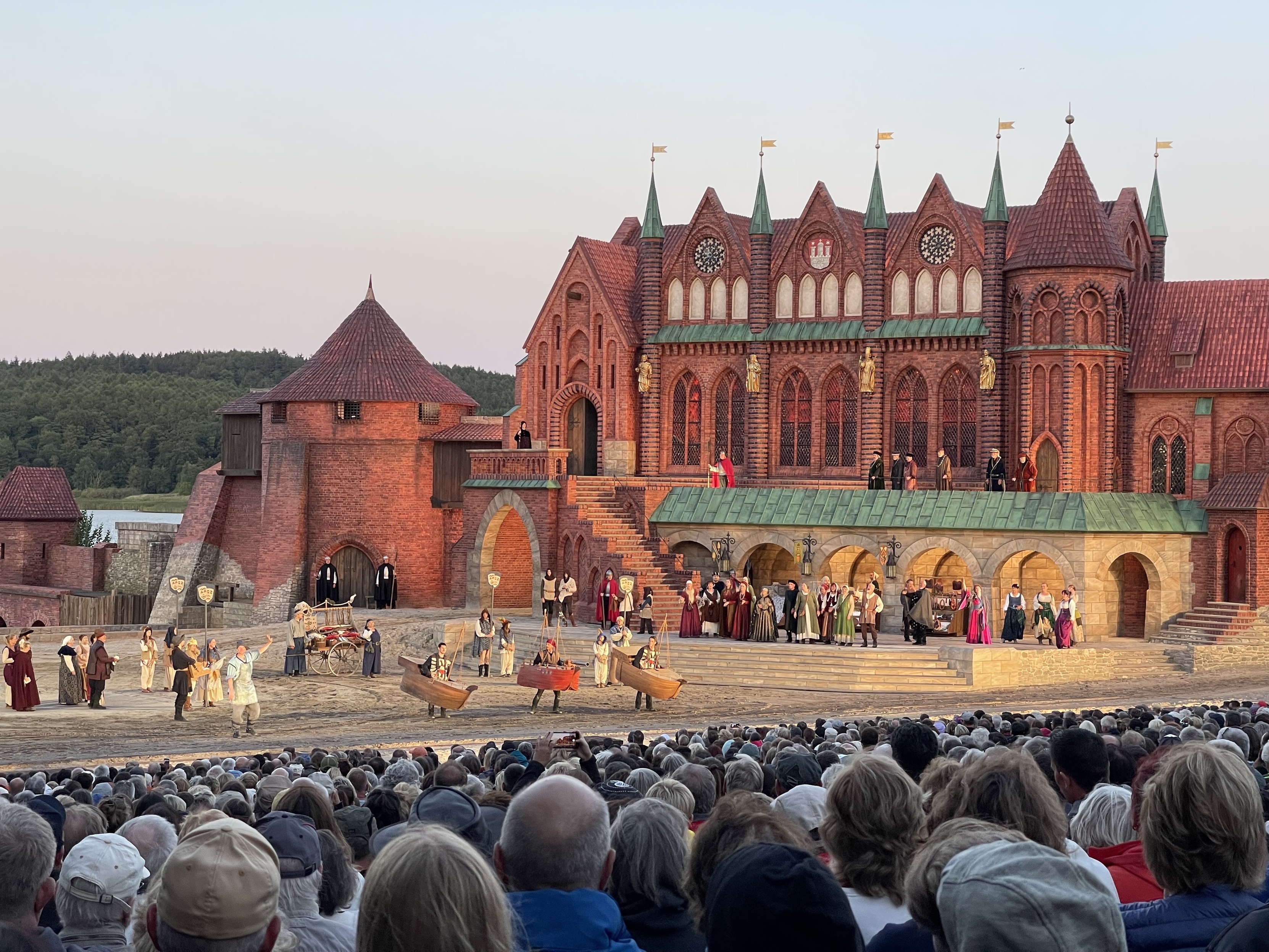 Theateraufführung im Freien vor einem großen Publikum mit Schauspielern in zeitlichen Kostümen auf einem burgähnlichen Set.