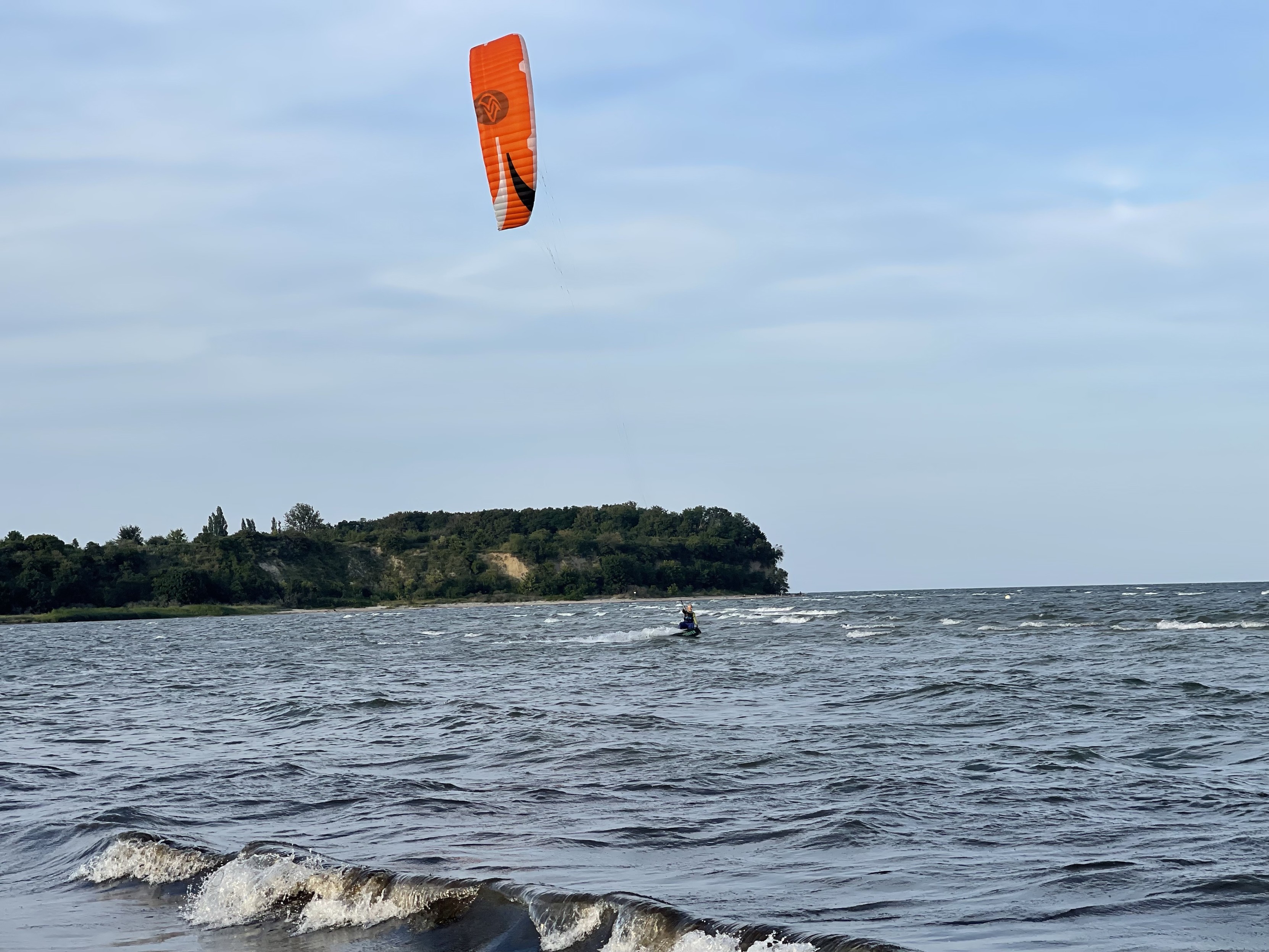 Eine Person, die im Ozean mit einer grünen bewaldeten Klippe im Hintergrund Kitesurft.