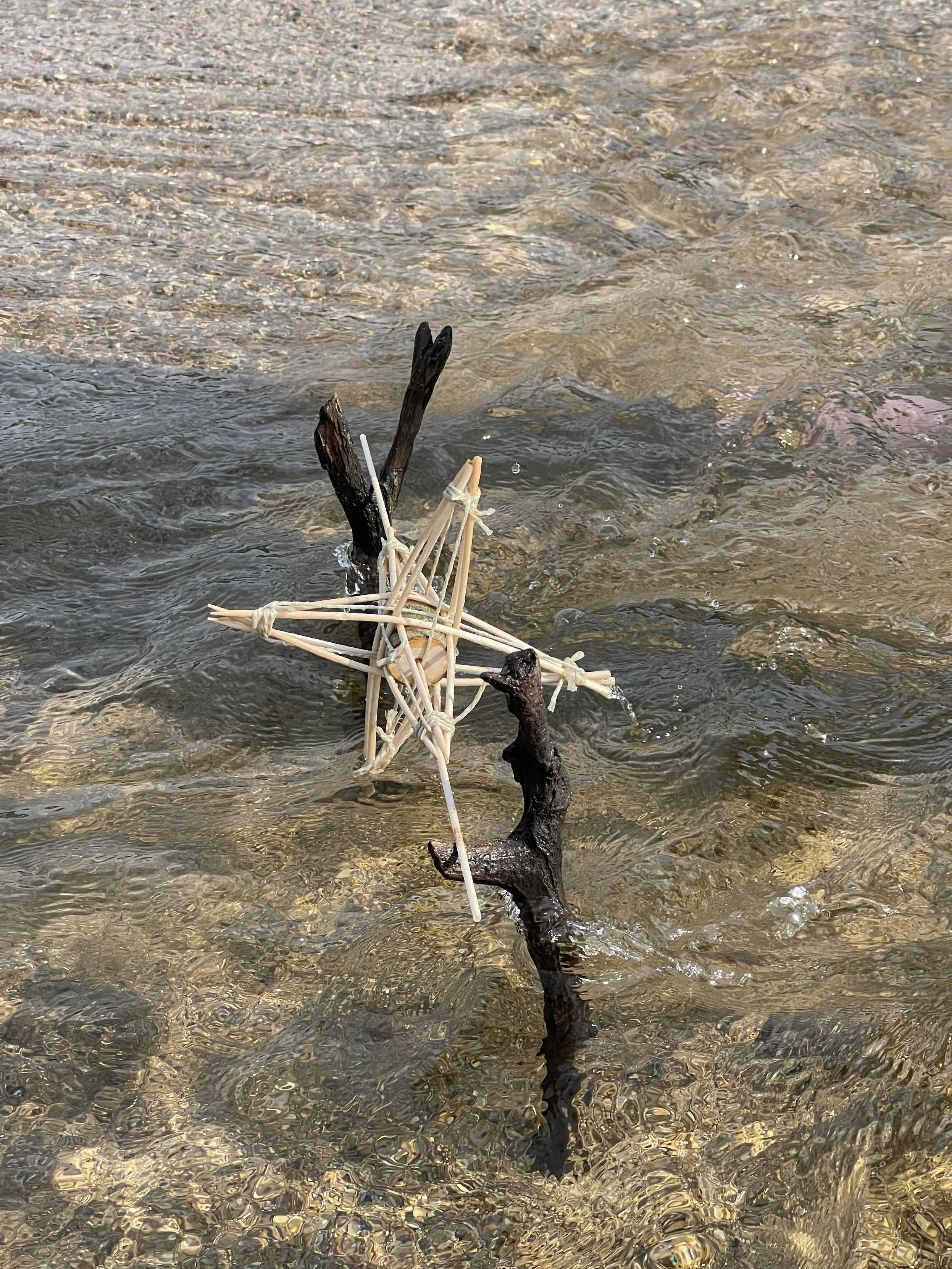 A wooden stick structure in the sand at a beach, partially submerged in shallow water.