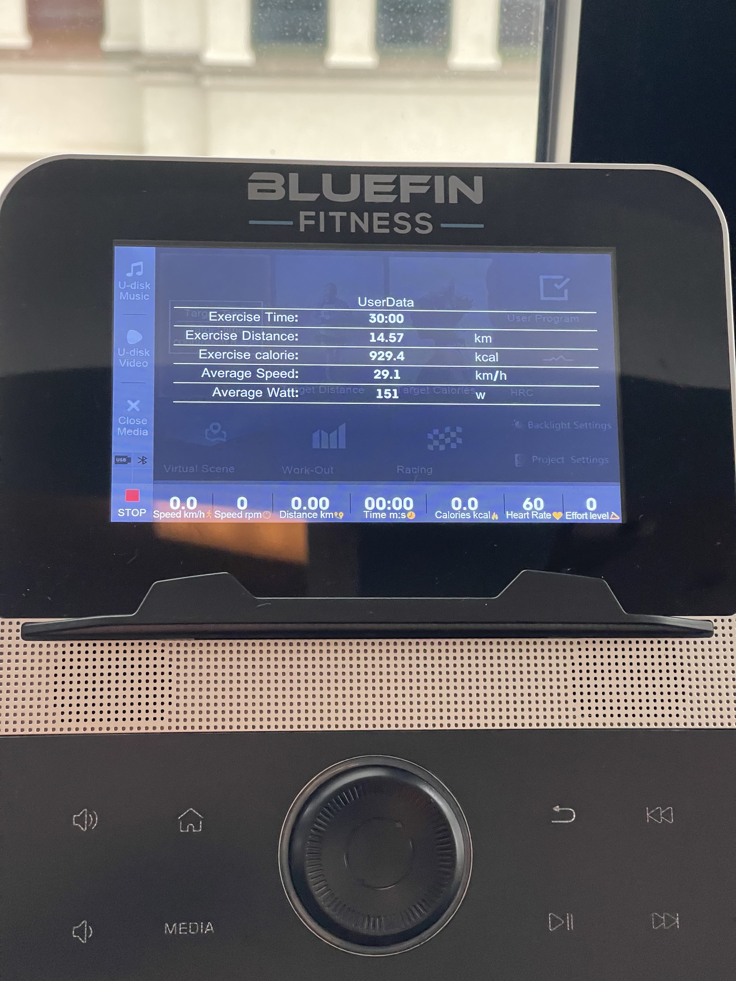 A display screen of a Bluefin Fitness exercise machine showing workout data, including time (30 min), distance 14.57 km), calories (929.4 kcal), average speed (29.1 km/h), and wattage (151 W).